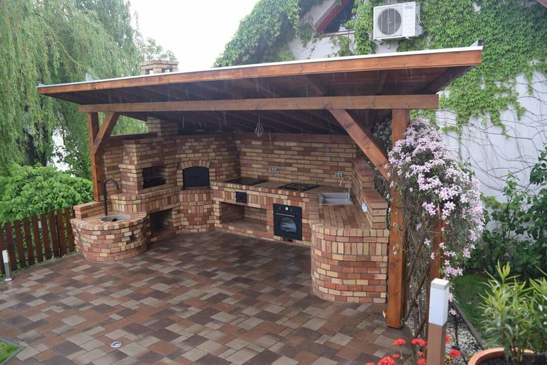  cocina al aire libre de ladrillo con un techo de madera, rodeada de vegetación y flores, destacando un ambiente acogedor y natural para cocinar al aire libre o relajarse.

Esta imagen es interesante porque combina el diseño arquitectónico con elementos naturales para crear un espacio al aire libre sereno y funcional. Espero que esta descripción sea útil para proporcionar una imagen mental clara del espacio representado.