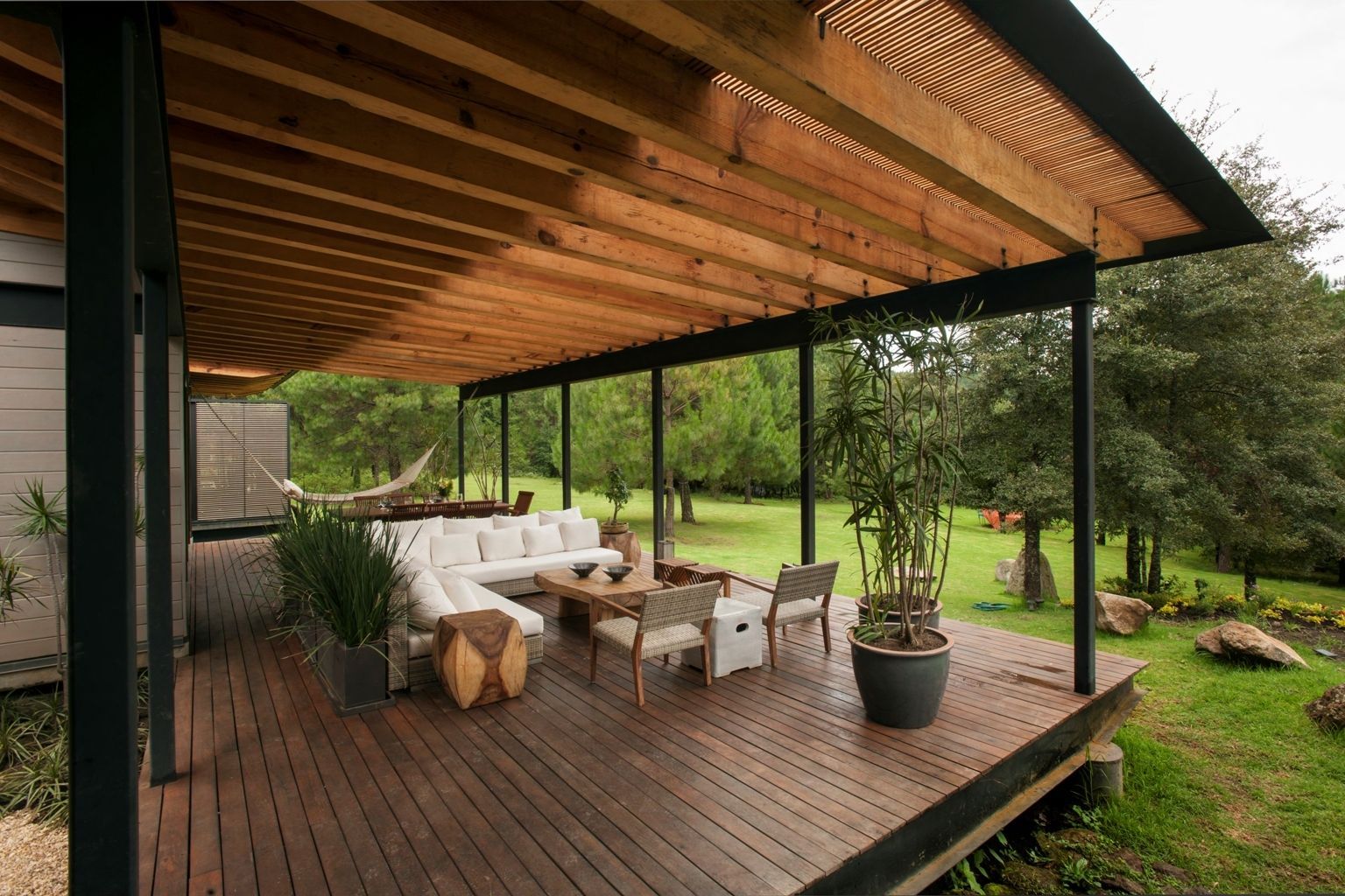 espacio de vida al aire libre sereno en una terraza de madera rodeada de vegetación exuberante, ofreciendo un entorno tranquilo para la relajación y la socialización.

La imagen muestra un área de estar al aire libre acogedora ubicada en una espaciosa terraza de madera, envuelta en la tranquilidad de la naturaleza.

Espero que esta descripción sea útil para proporcionar una imagen mental clara del espacio representado.