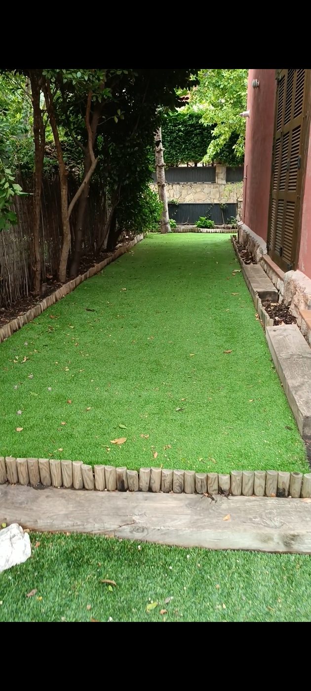 Césped artificial instalado en el jardín lateral con bordillos de madera