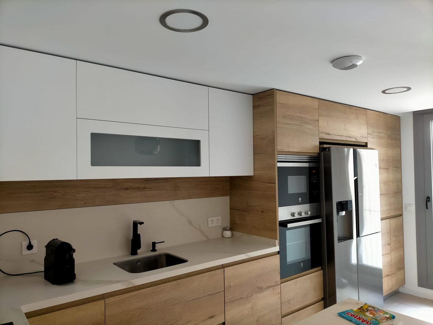 Cocina terminada en blanco y madera con grifería negra y electrodomésticos integrados