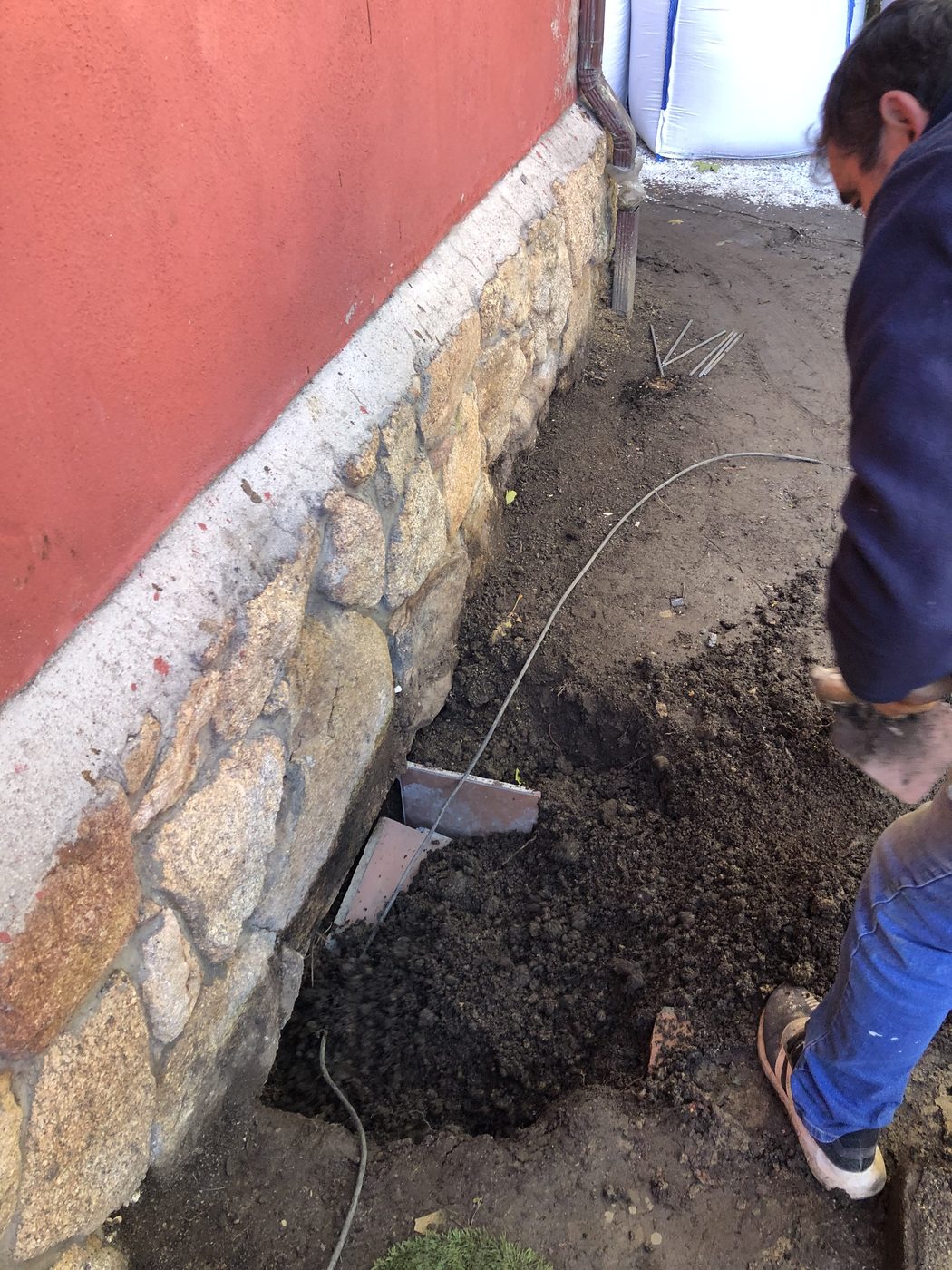 Excavación de zanja junto a la fachada de piedra de la vivienda